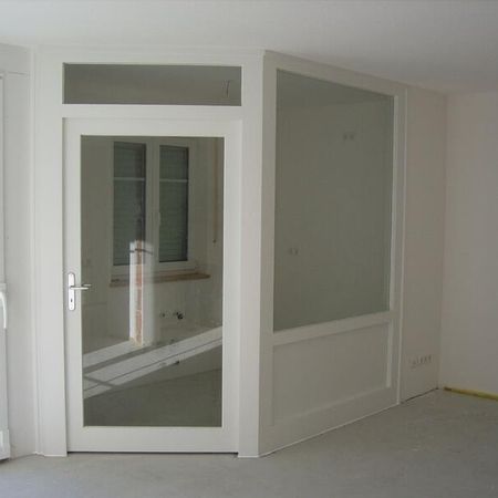 Ein Raum mit einer weißen Tür und einem Fenster, das Tageslicht hereinlässt